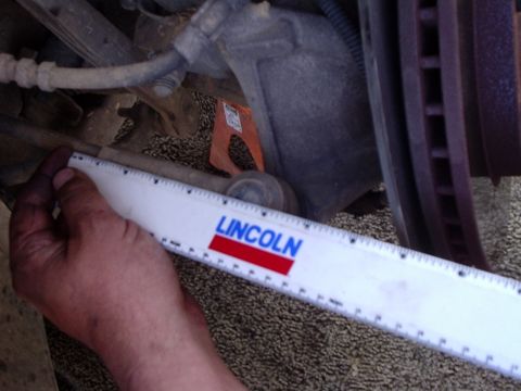 2000 Ford Taurus - A ruler branded with 'Lincoln' is used to measure a suspension component, likely for a repair or diagnostic.