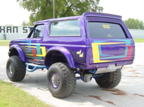 1991 Ford Bronco - This heavily modified Ford Bronco features a vibrant purple paint job with colorful geometric decals and oversized off-road tires.