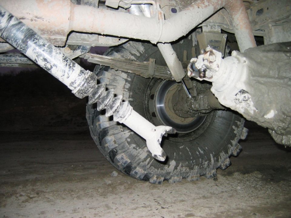 Muddy front hub, brake rotor, and off-road tire viewed from under a lifted vehicle