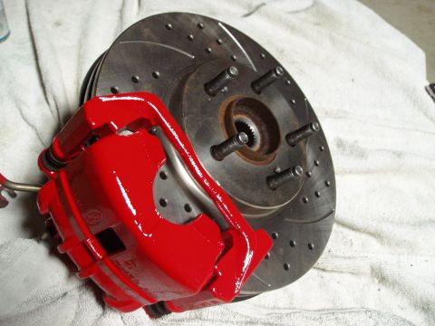 1993 Ford Taurus - A freshly painted red brake caliper is shown next to a drilled and slotted brake rotor.