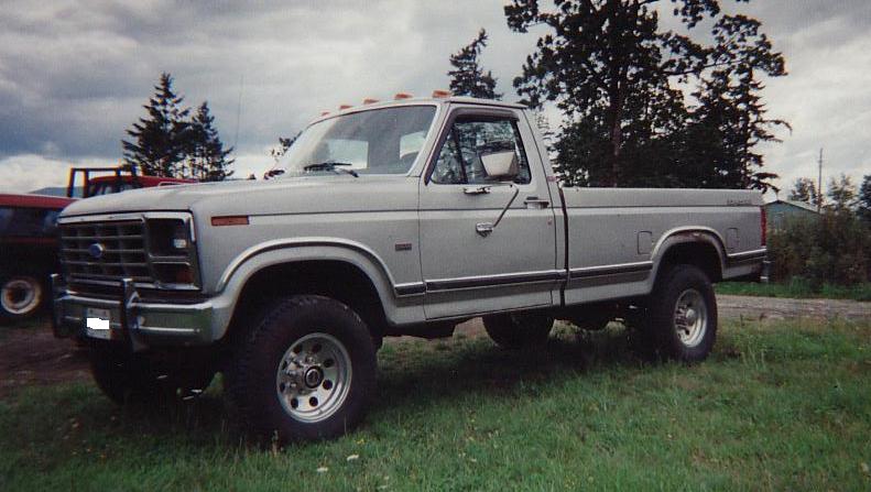 Silver Ford regular cab long-bed pickup with roof lights and alloy wheels parked on grass, front three-quarter view