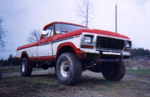 1979 Ford F-250 - A lifted red and white pickup truck sits parked outdoors on a dirt lot.