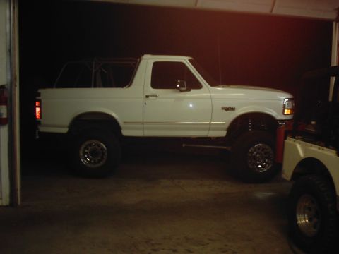 1978 Ford Bronco - White Ford Bronco with a roll cage and lifted suspension is parked indoors next to another vehicle.