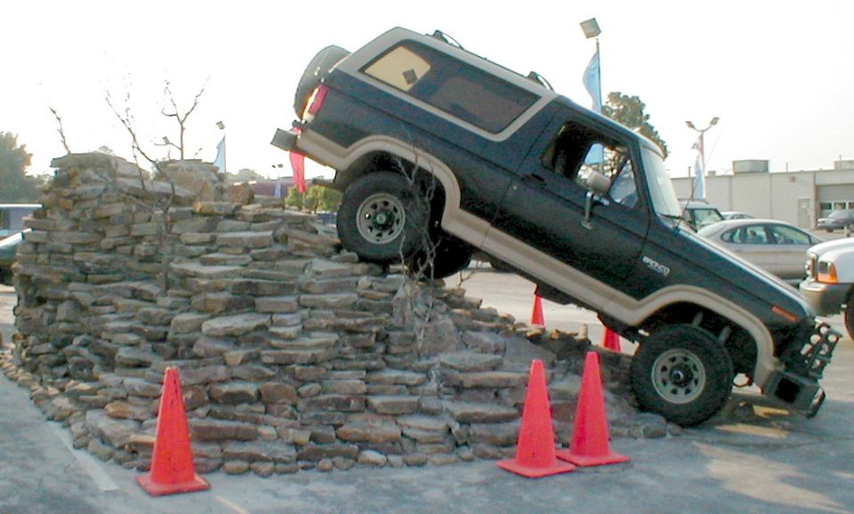 Dark Ford Bronco SUV climbing a rock pile at steep angle with orange cones nearby