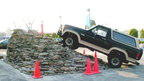 1983 Ford Bronco - A Ford Bronco navigates an artificial rock obstacle course with orange cones and flags visible.