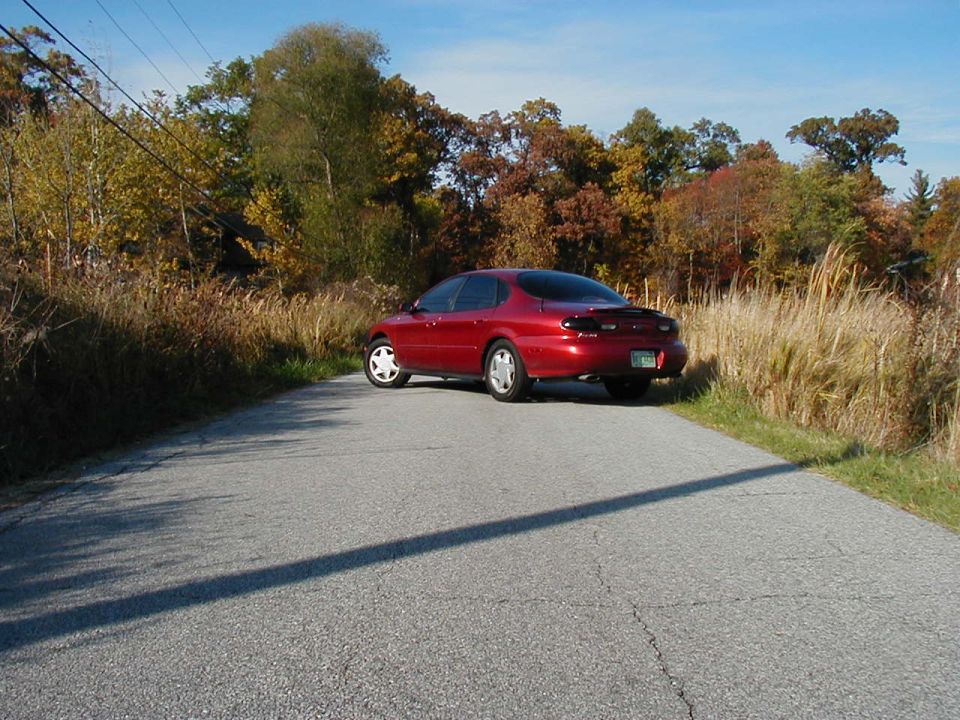1997 Ford Taurus sedan parked on a paved road with autumn foliage in the background