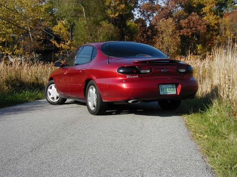 1997 Ford Taurus - A red sedan is parked on the side of a road during the autumn season.