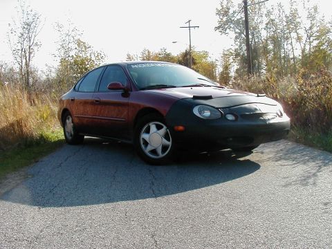 1997 Ford Taurus - A maroon sedan, likely a 1996 model, is parked on the side of a road with a car bra covering its front.