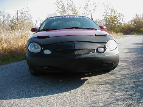 1997 Ford Taurus - A red 1997 Ford Taurus is seen from the front, partially covered by a black car bra and a windshield banner.