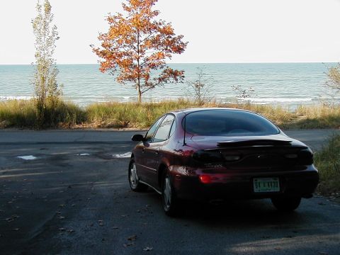 1997 Ford Taurus - A maroon sedan is parked near a body of water with trees in the background.