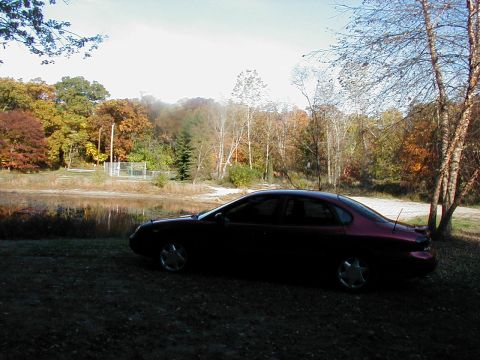 1997 Ford Taurus - A 1997 Ford Taurus sits by a lake during the fall season, with colorful trees surrounding the area.