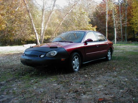 1997 Ford Taurus - A maroon sedan is parked outdoors, partially covered by a black car bra, with autumn foliage visible.