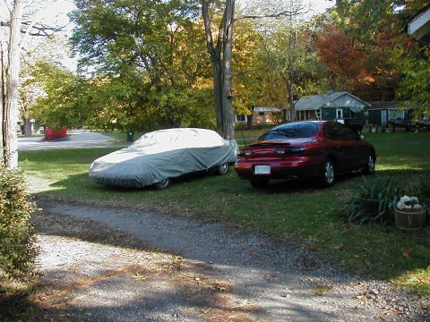1997 Ford Taurus - A red 1997 Ford Taurus coupe is parked in a grassy yard next to a car covered with a tarp.