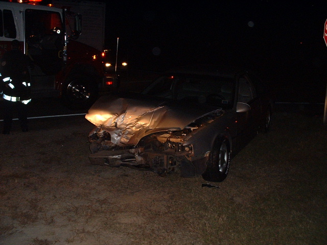 1989 Ford Thunderbird wrecked in front, fire truck behind it at night