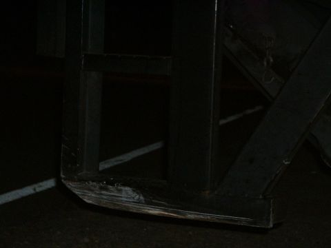 1989 Ford Thunderbird - A dark, industrial scene focuses on the lower corner of a metal frame, showing signs of wear and tear.