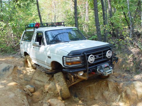 1996 Ford Bronco - This 1996 Ford Bronco is navigating a challenging off-road obstacle with its tires on rocks and mud.