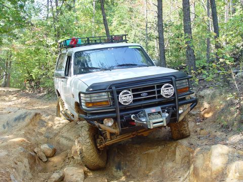1996 Ford Bronco - This white Ford Bronco is tackling a challenging off-road course with its specialized equipment.