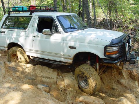 1996 Ford Bronco - This 1996 Ford Bronco is captured mid-action, tackling a challenging off-road obstacle with its tires deep in mud and rocks.