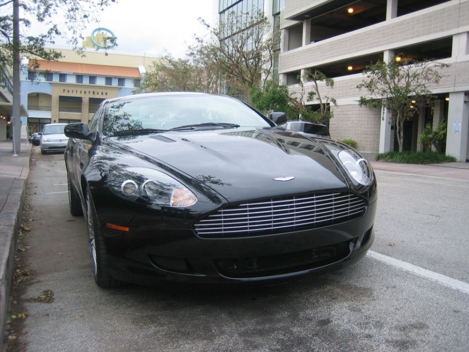Black Aston Martin DB9 coupe front three-quarter parked on a street near a parking garage
