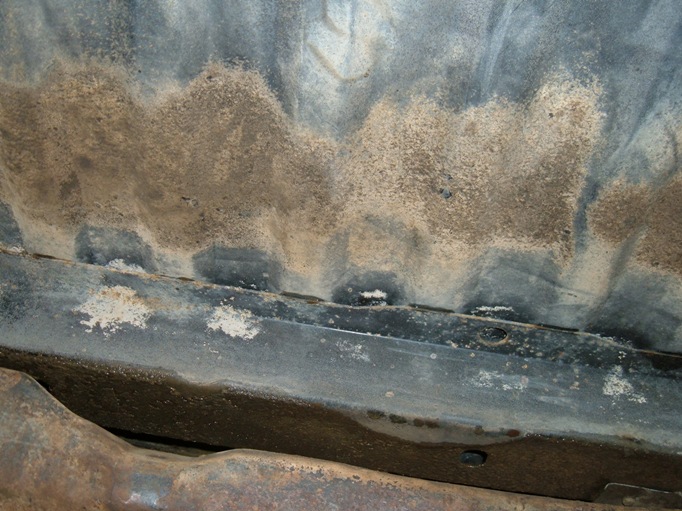 Corroded vehicle underbody panel with rust and white powdery deposits along a seam