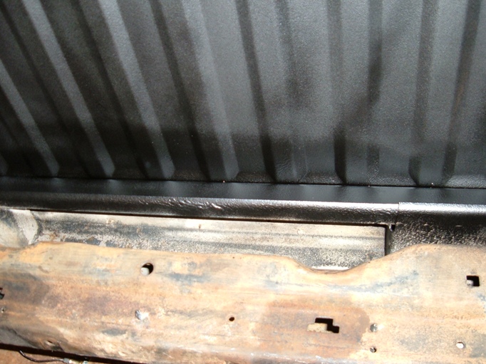 Close-up of black ribbed panel above rusty bed rail with mounting holes