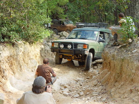 1996 Ford Bronco - Multiple off-road vehicles are seen on a challenging dirt trail with spectators observing the action.