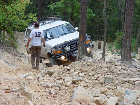 1996 Ford Bronco - This SUV is navigating a challenging off-road trail with a person observing its progress.