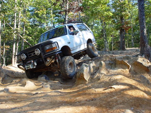 1996 Ford Bronco - A white 1992 Ford Bronco navigates a challenging rocky off-road course surrounded by trees.