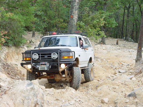 1996 Ford Bronco - A white 1996 Ford Bronco tackles a challenging off-road course with large tires and a modified front end.