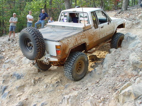 1996 Ford Bronco - A white pickup truck navigates a challenging rocky terrain, with a spare tire mounted on its rear.
