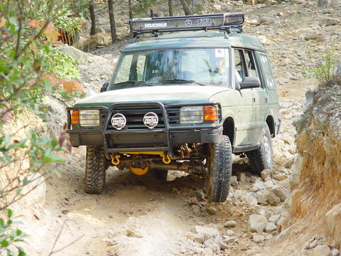 1996 Ford Bronco - This off-road SUV navigates a challenging rocky terrain, equipped with a bull bar and roof rack for adventure.