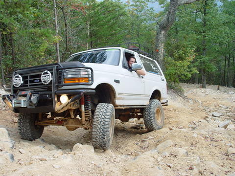1996 Ford Bronco - A white Ford Bronco navigates a rocky off-road trail in a wooded area.
