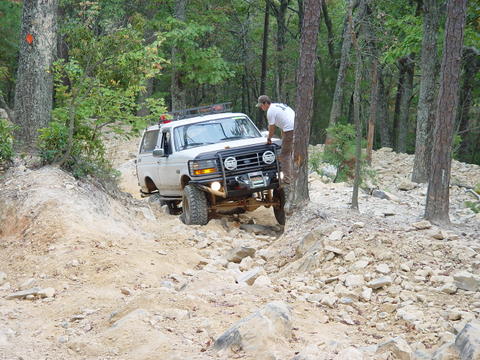 1996 Ford Bronco - This SUV navigates a challenging, rocky off-road path surrounded by trees.