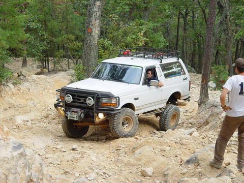 1996 Ford Bronco - A white Ford Bronco navigates a rocky off-road trail, with a person watching.