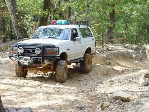 1996 Ford Bronco - White 1996 Ford Bronco navigates a challenging off-road course with large tires and a roof rack.