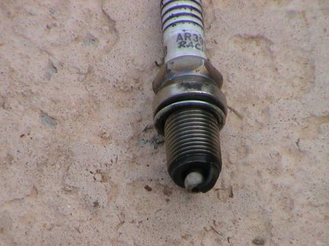 1979 Ford Bronco - A close-up view of a spark plug, identified as AR39 RACING, rests on a rough, light-colored surface.