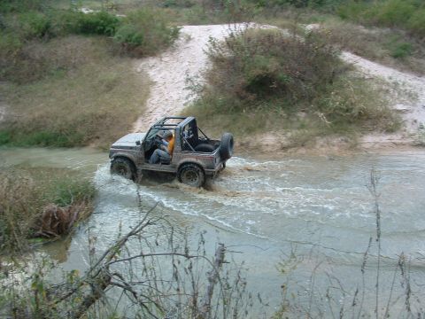 1993 Ford Bronco - A 4x4 vehicle navigates through a muddy water crossing on an off-road trail.
