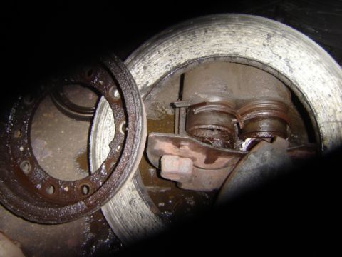 1992 Ford Bronco - Close-up of a corroded vehicle brake assembly, showing worn parts and fluid leakage.