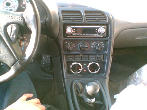 1997 Ford Probe - Interior center stack of a car showing an aftermarket CD head unit above rotary HVAC controls, two round aftermarket gauges below, and a ma…