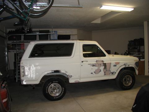 1986 Ford Bronco - Side profile of a white 1986 Ford Bronco with decals on the door, parked inside.