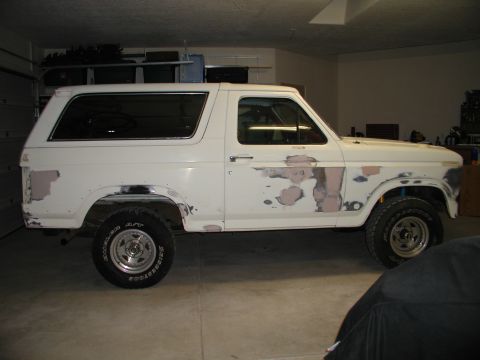 1986 Ford Bronco - A white SUV is parked inside a garage, showing its side profile with some decals on the door.