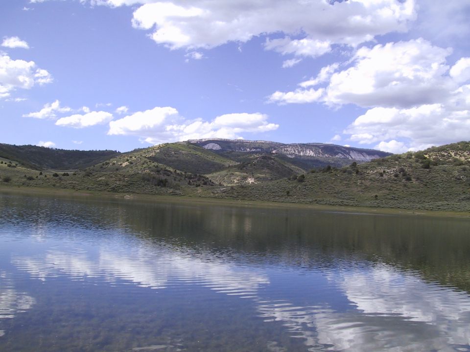 Calm lake with sky reflection, green hills and cliffs behind