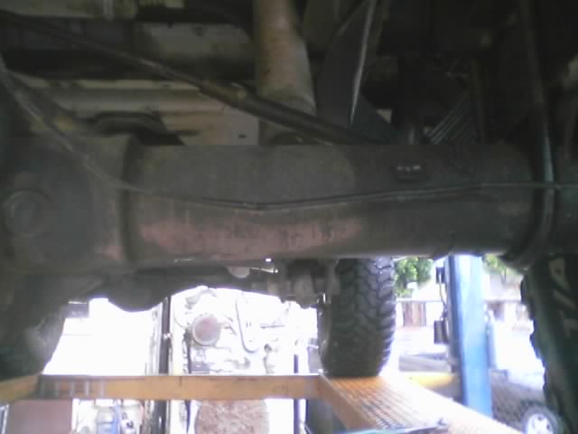 Underside view of a rear axle and driveshaft with tire visible, vehicle on a shop lift