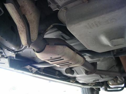 1999 Ford Crown Victoria - The underside of a vehicle is shown, with focus on the exhaust system and a component bearing the Ford logo.