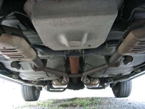 1999 Ford Crown Victoria - A view of the underside of a vehicle, showing the exhaust pipes, catalytic converters, and part of the drivetrain.