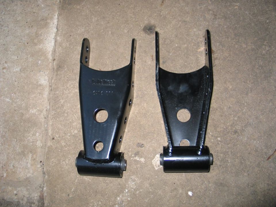 Pair of black steel suspension shackle brackets with bushings on a concrete floor