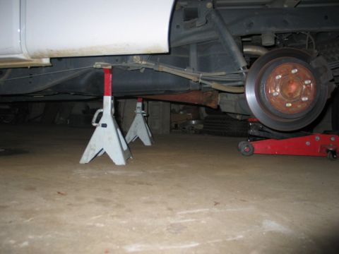2004 Ford F-150 - The rear wheel of a white pickup truck is removed while it is supported by jack stands and a floor jack for maintenance.