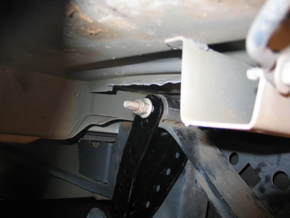 Underbody view of a black bracket bolted to a truck frame with a threaded stud and nut