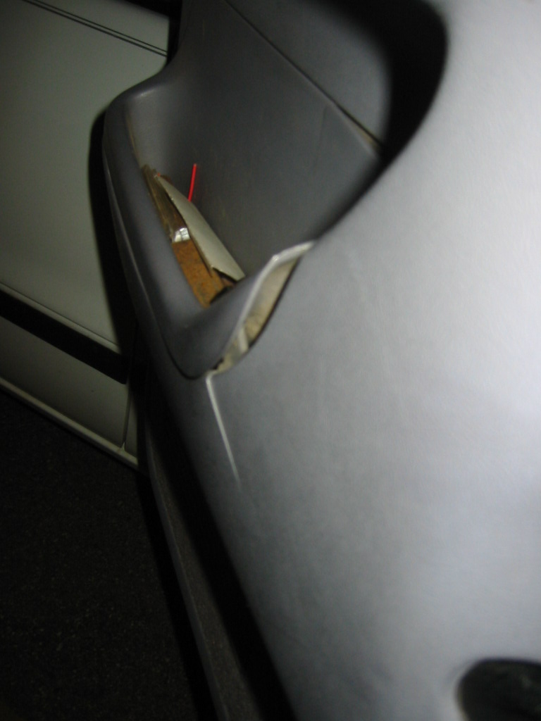 Close-up of a torn gray interior trim panel revealing wood and a red marker underneath