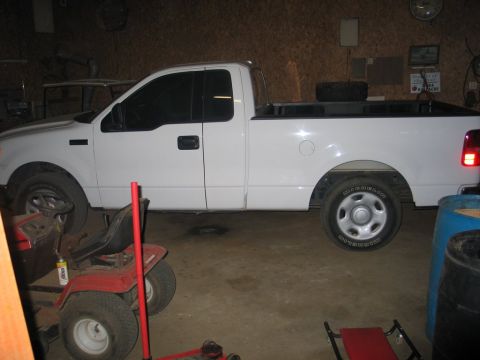 2004 Ford F-150 - A white 2004 Ford F-150 pickup truck is parked in a garage, with a red riding mower nearby.